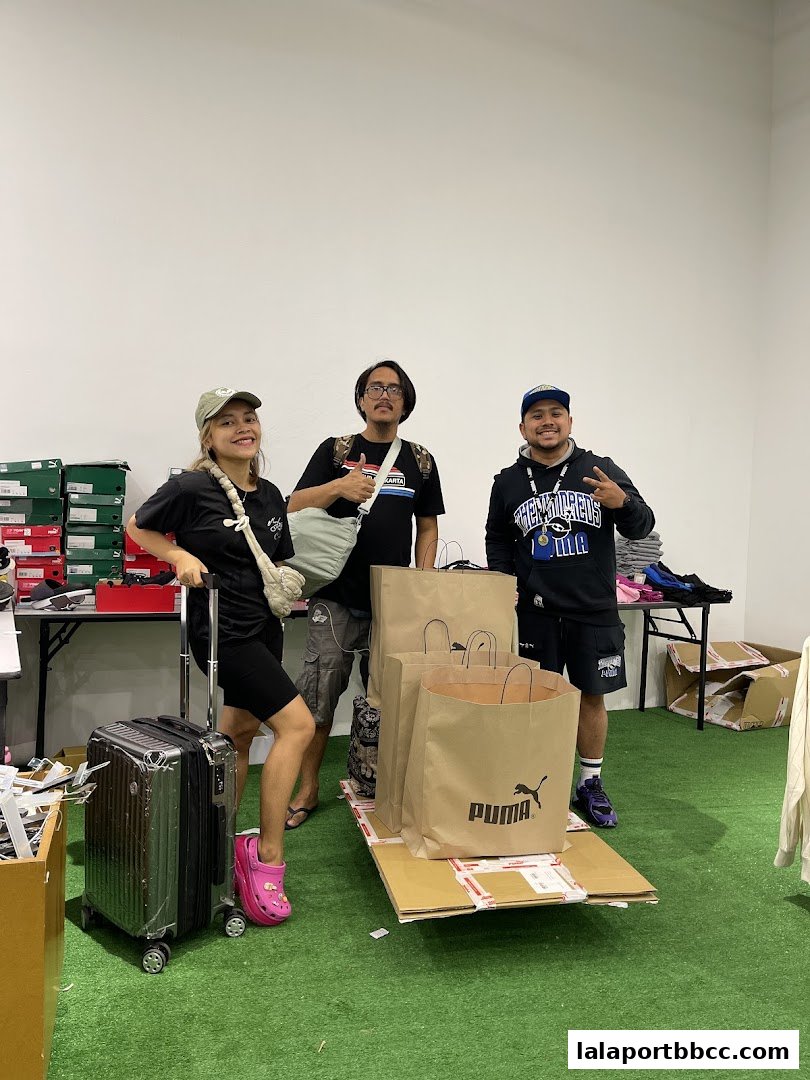 Three people posing with Puma shopping bags and luggage in a store.