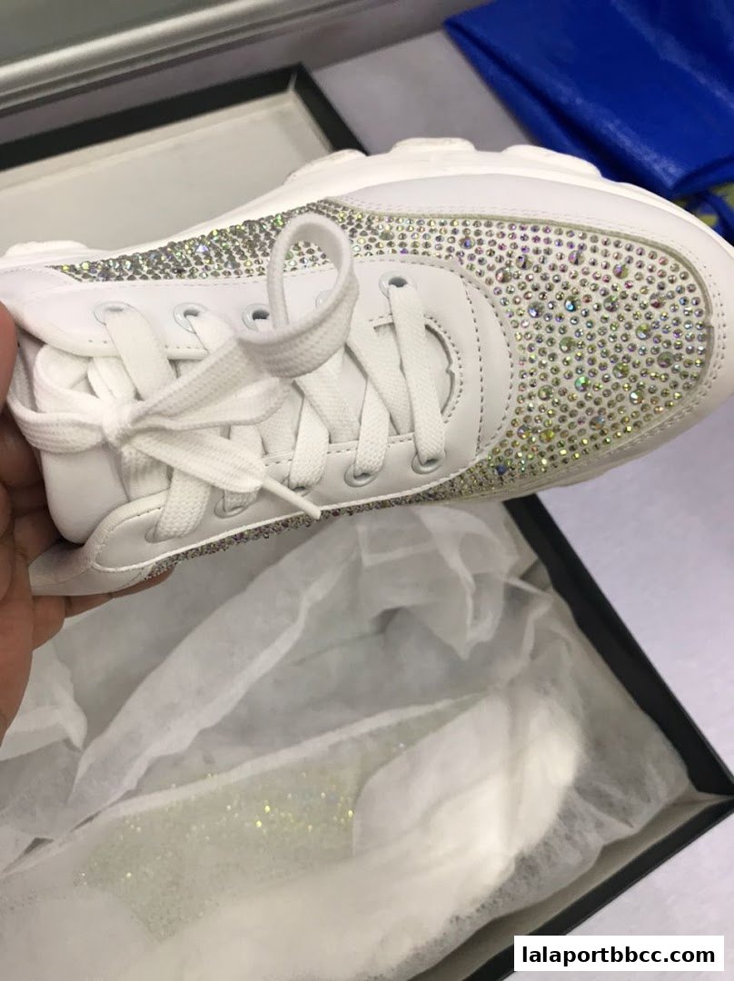 A hand holds a white sneaker adorned with sparkling rhinestones, presented in a box.