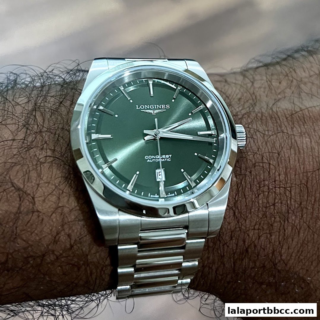 A close-up shot of a Longines Conquest Automatic watch with a green dial on a wrist.