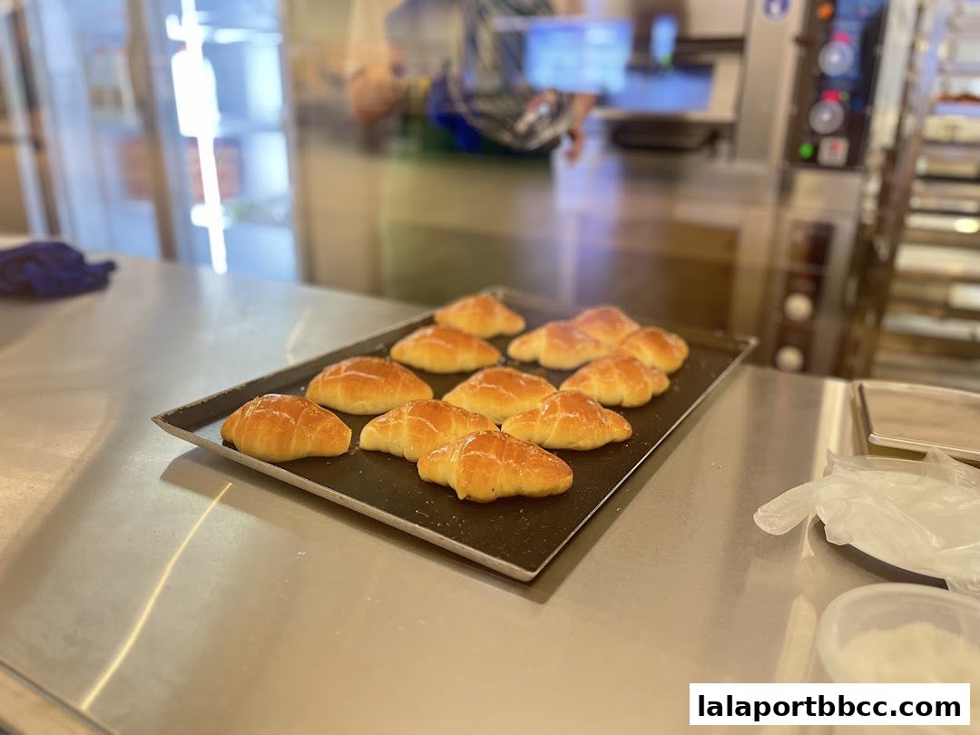 A baking tray filled with freshly baked croissants on a stainless steel counter.