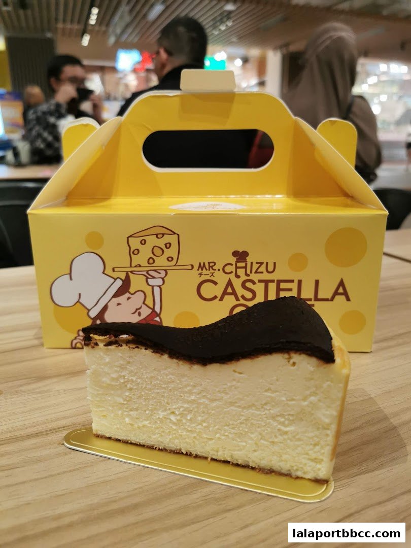 A slice of burnt cheesecake from Mr. Chizu Castella with its branded yellow box.
