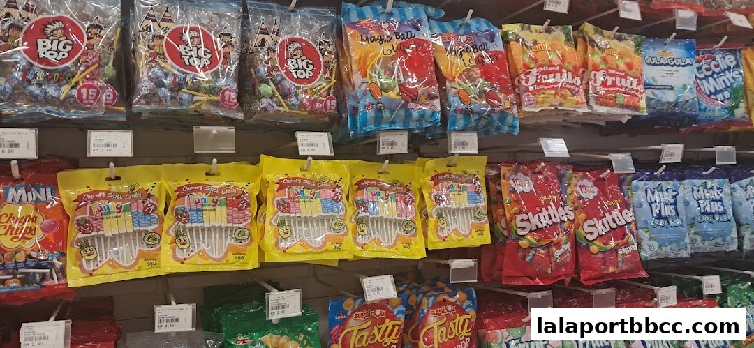 A display of various candies and lollipops on shelves, including Big Top, Chupa Chups, and Skittles.