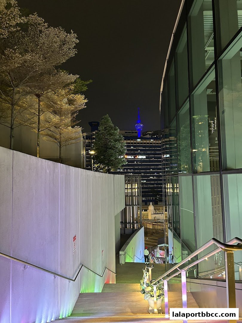 A nighttime view of a modern staircase with colorful lights leading to a city skyline.