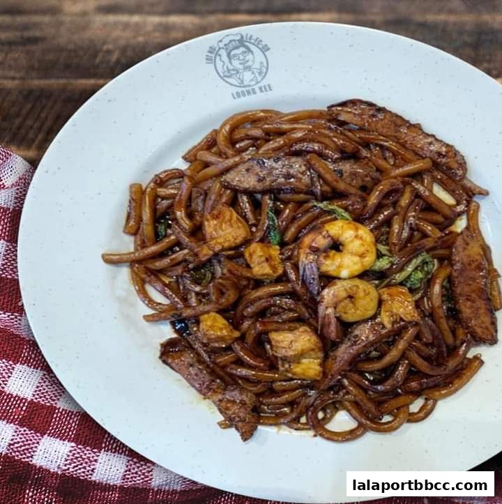 A plate of Hokkien Mee with prawns, meat, and vegetables on a wooden table.