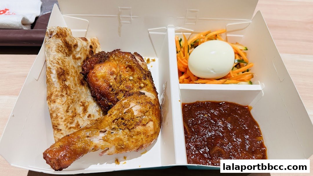 A takeaway box filled with a chicken leg, roti, salad, and sambal.