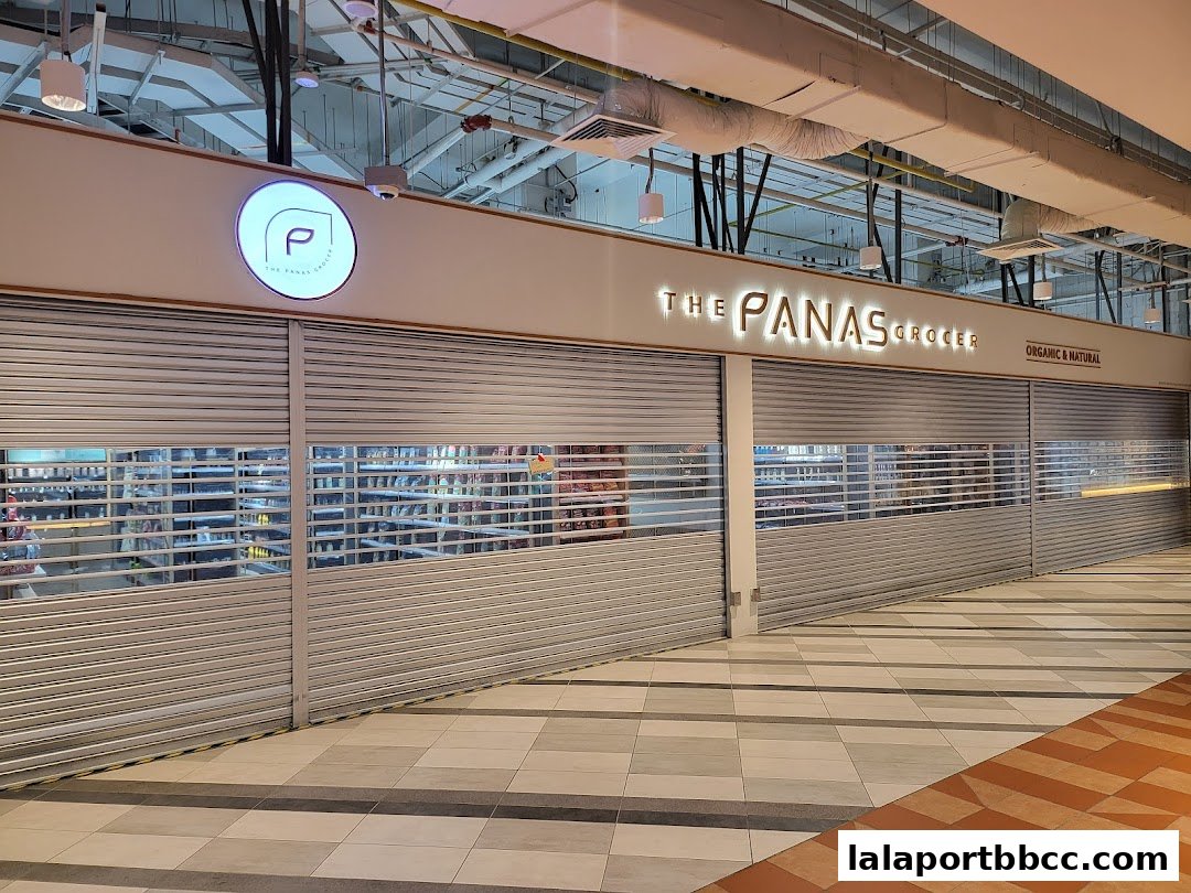 The Panas Grocer shop front with closed roller shutters and illuminated signage.