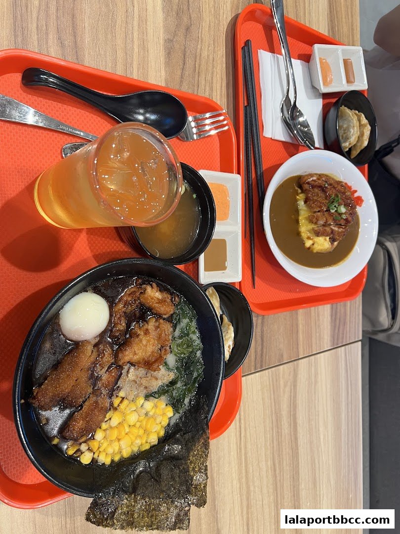Two trays of Japanese food, including ramen, curry rice, and gyoza, are displayed on a wooden table.