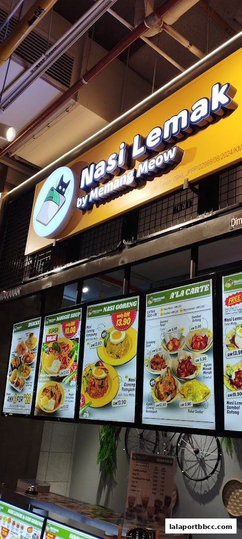 A food court stall with illuminated menus displaying various Malaysian dishes and drinks.