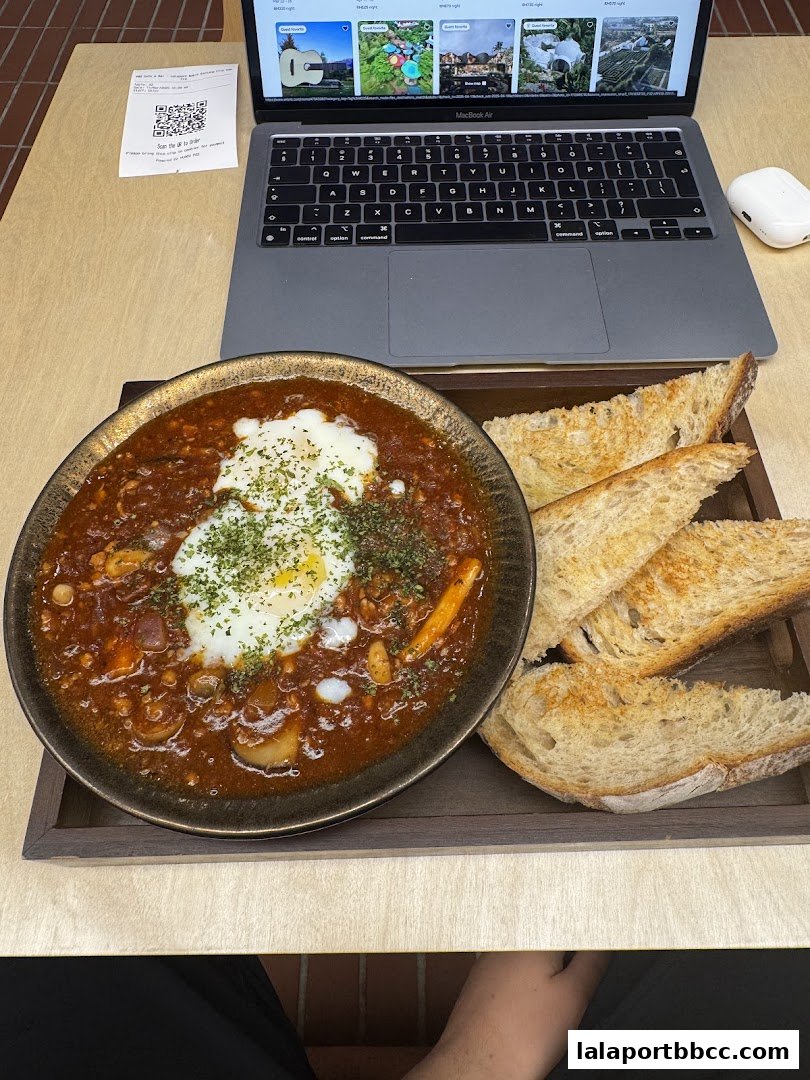 A hearty stew with a fried egg and toast served with a laptop and receipt.