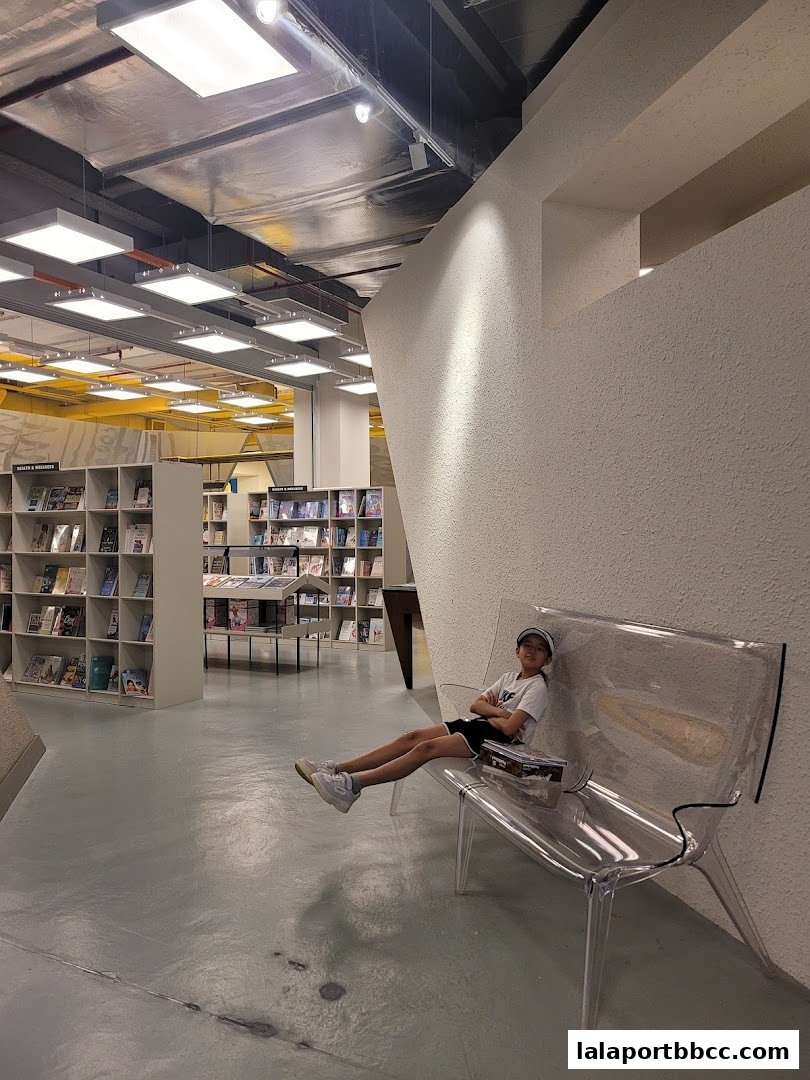 A child sits on a clear bench in a modern bookstore with shelves of books visible.