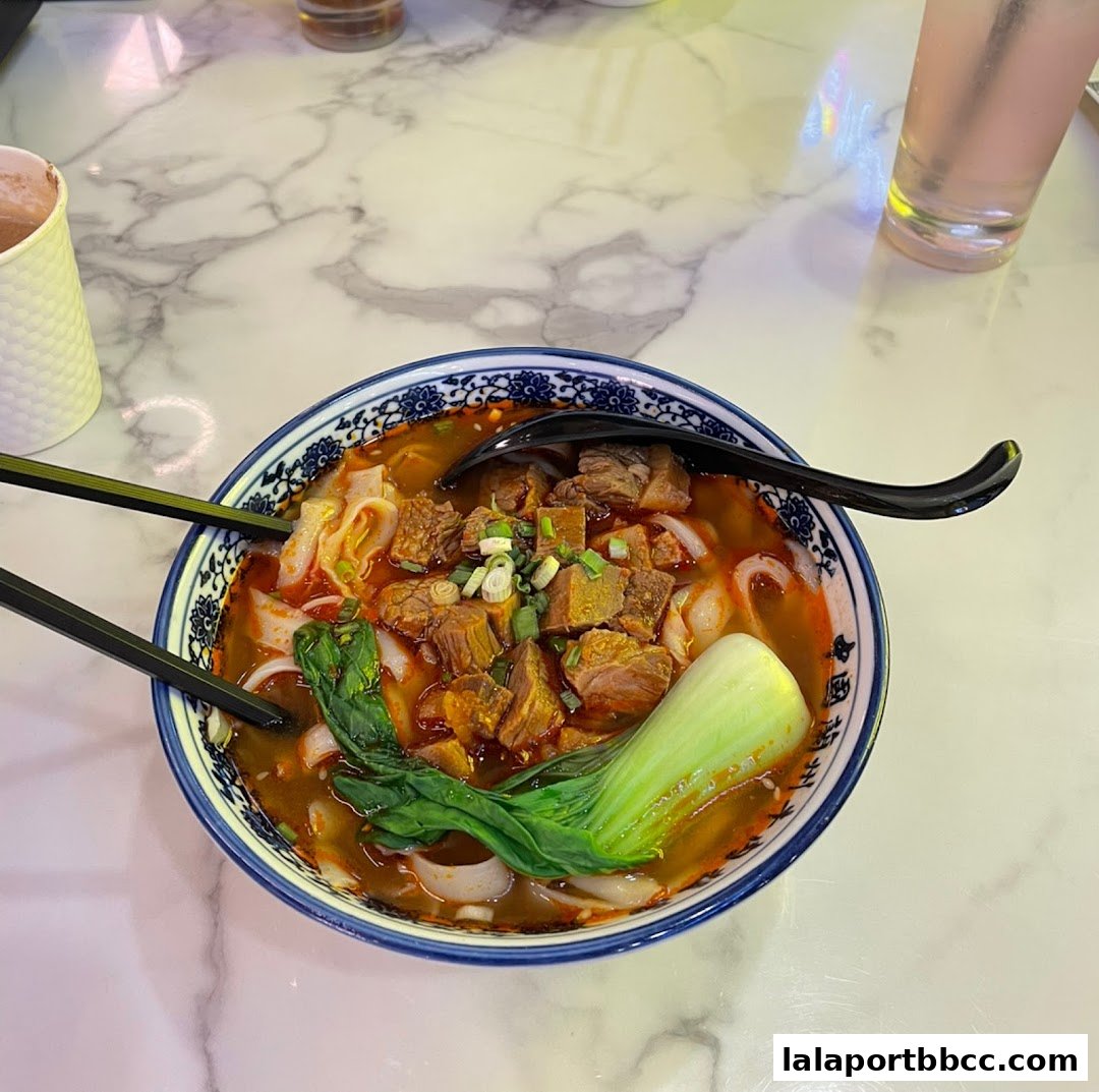 A steaming bowl of beef noodle soup with bok choy and chopsticks.