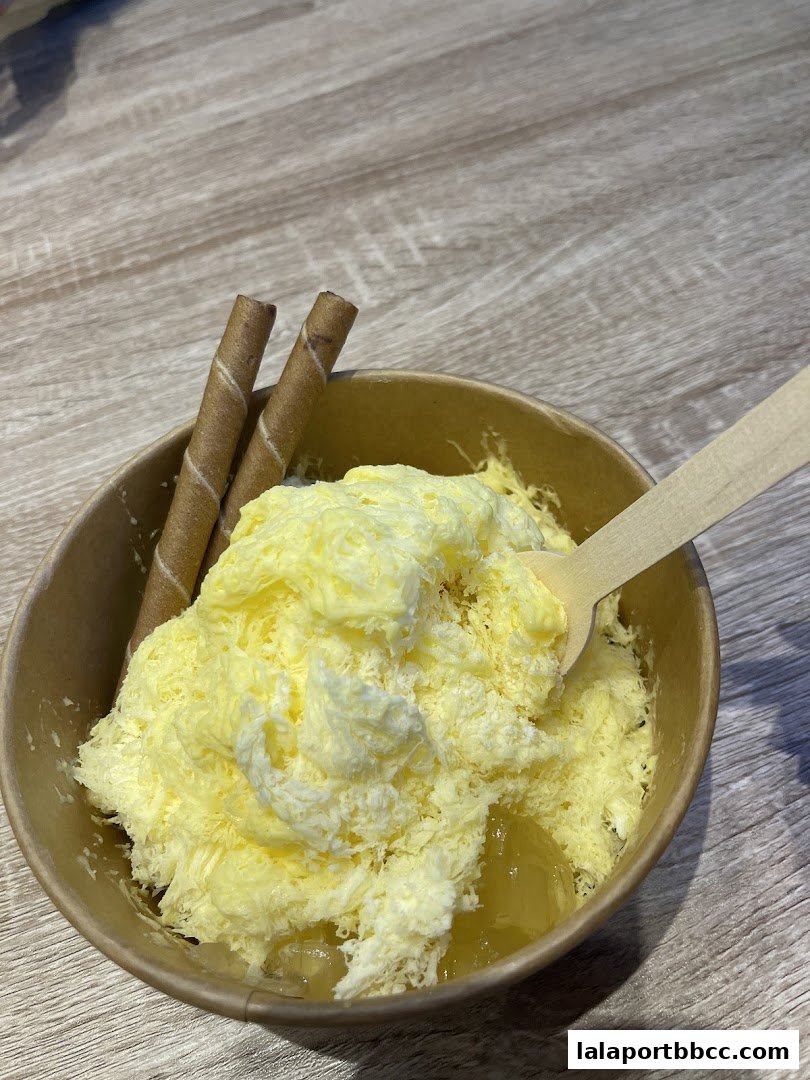 A close-up of a yellow shaved ice dessert with wafer sticks and a wooden spoon.