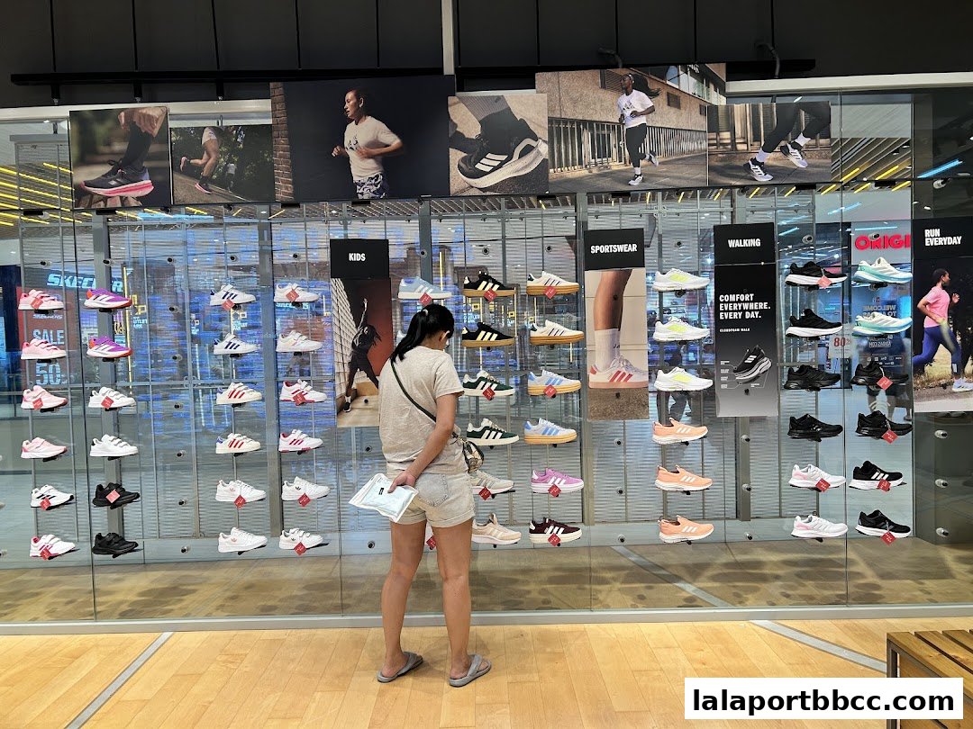A customer browses a wide selection of Adidas sneakers displayed on shelves in a brightly lit store.