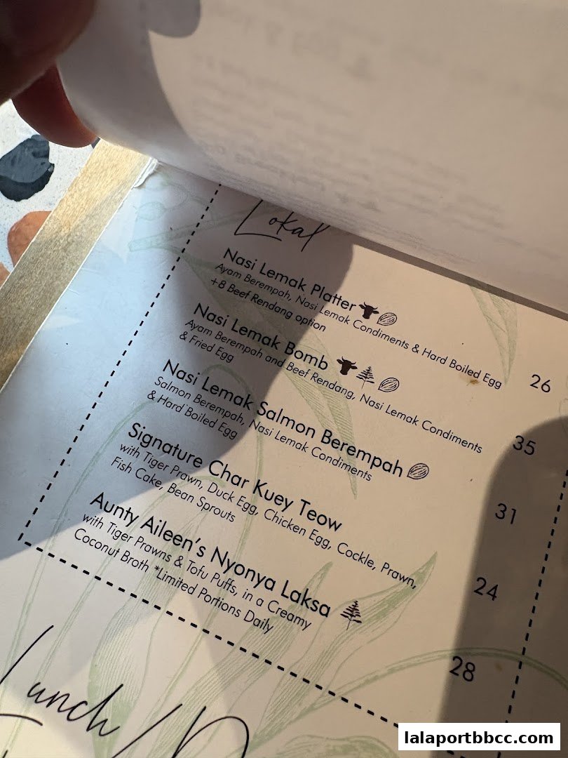 A close-up view of a menu from POKOK LaLaport, showcasing various Malaysian dishes.