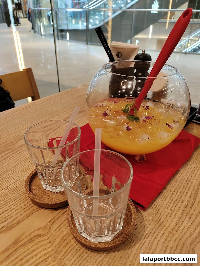 A large bowl of yellow beverage with ice, fruit, and a red spoon, served with two glasses.