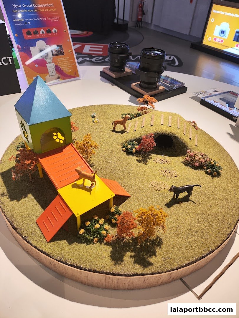 A miniature diorama of a dog park with a dog house, agility equipment, and animal figures.