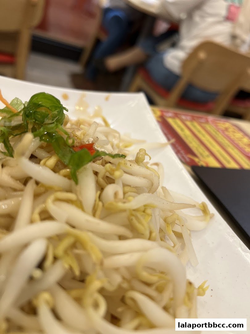 A close-up of a plate of bean sprouts with garnishes, in a restaurant setting.