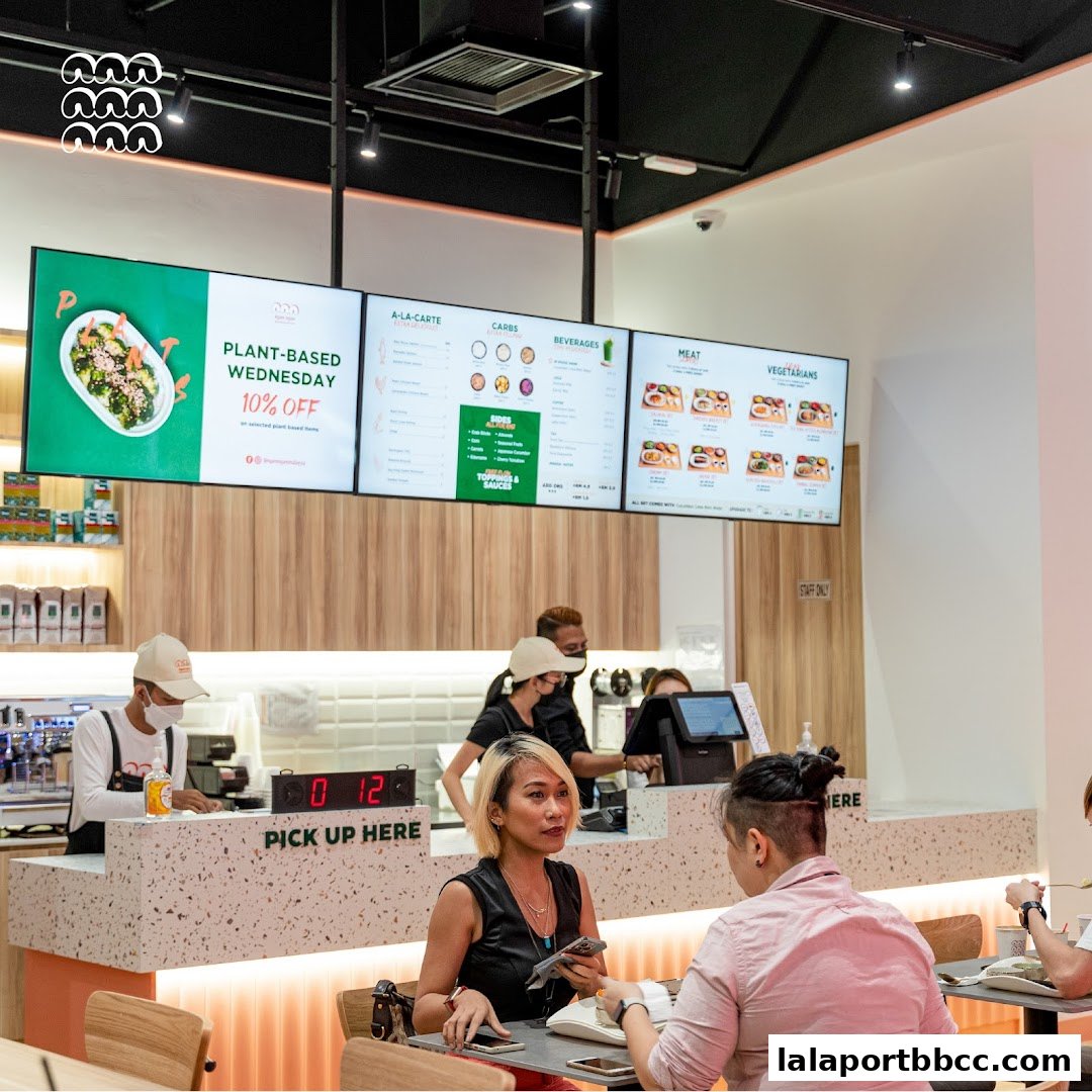 Customers ordering at a counter with digital menus displaying food options and promotions.