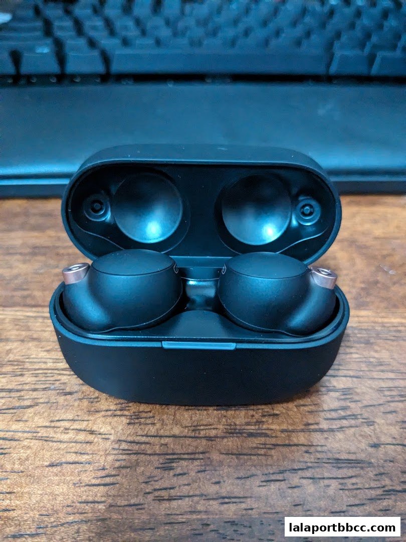 A pair of black Sony wireless earbuds in their charging case on a wooden surface.