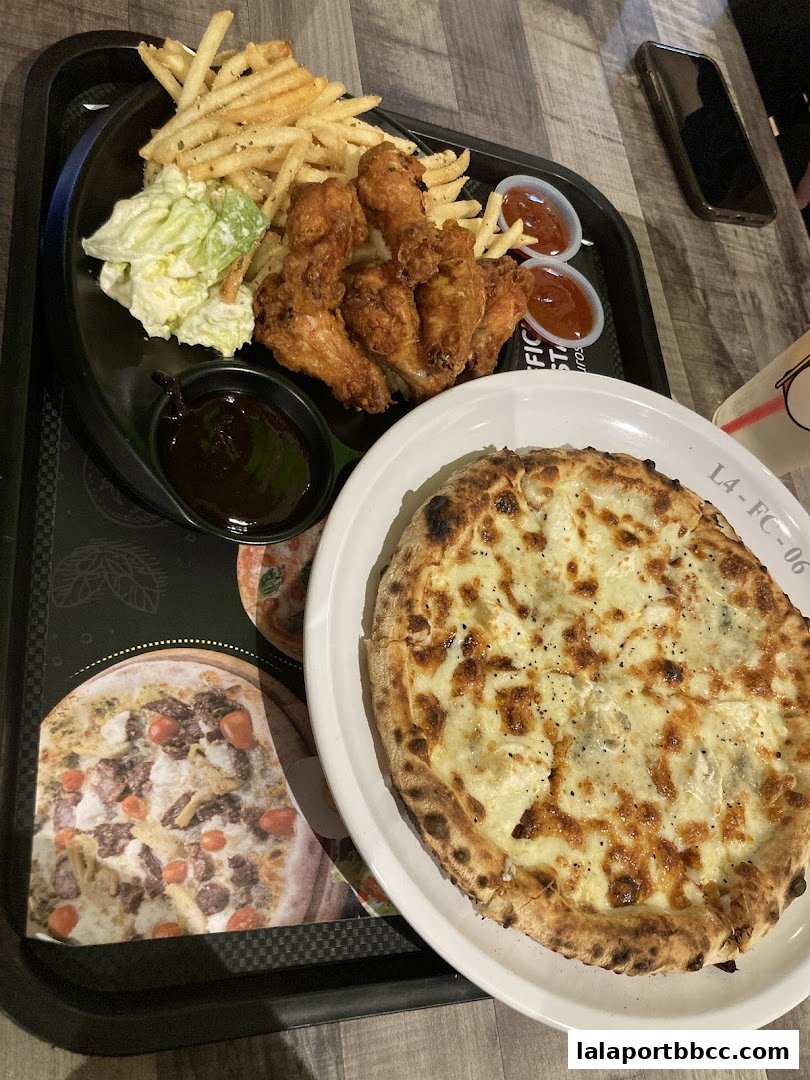 A delicious meal featuring fried chicken wings, french fries, coleslaw, and a gourmet pizza.