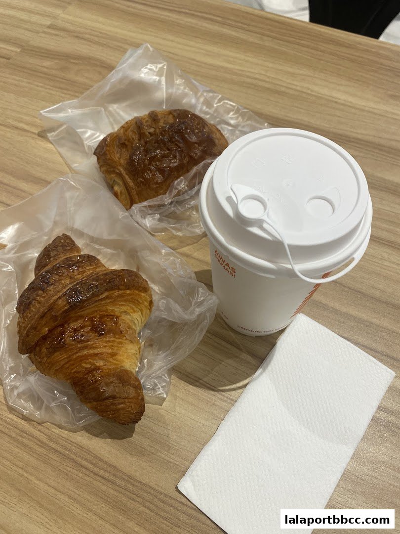 Two croissants and a coffee cup with a napkin on a wooden table.