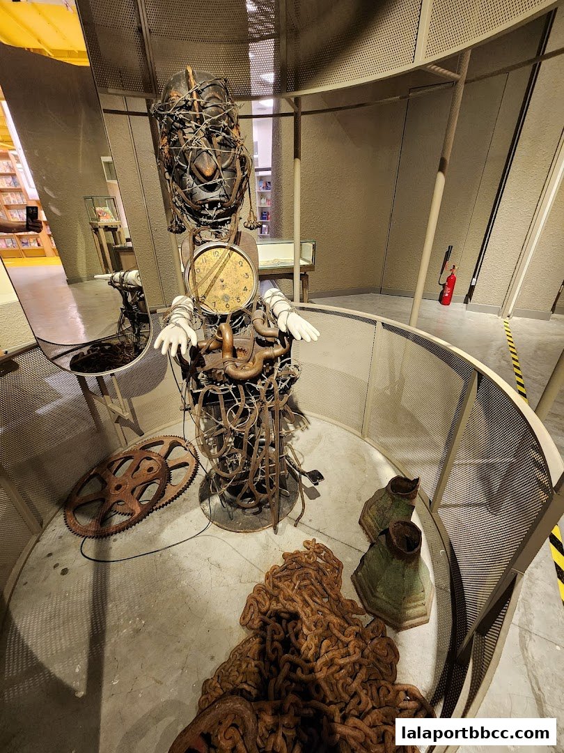 An artistic sculpture made of metal and a clock is displayed in a circular enclosure.