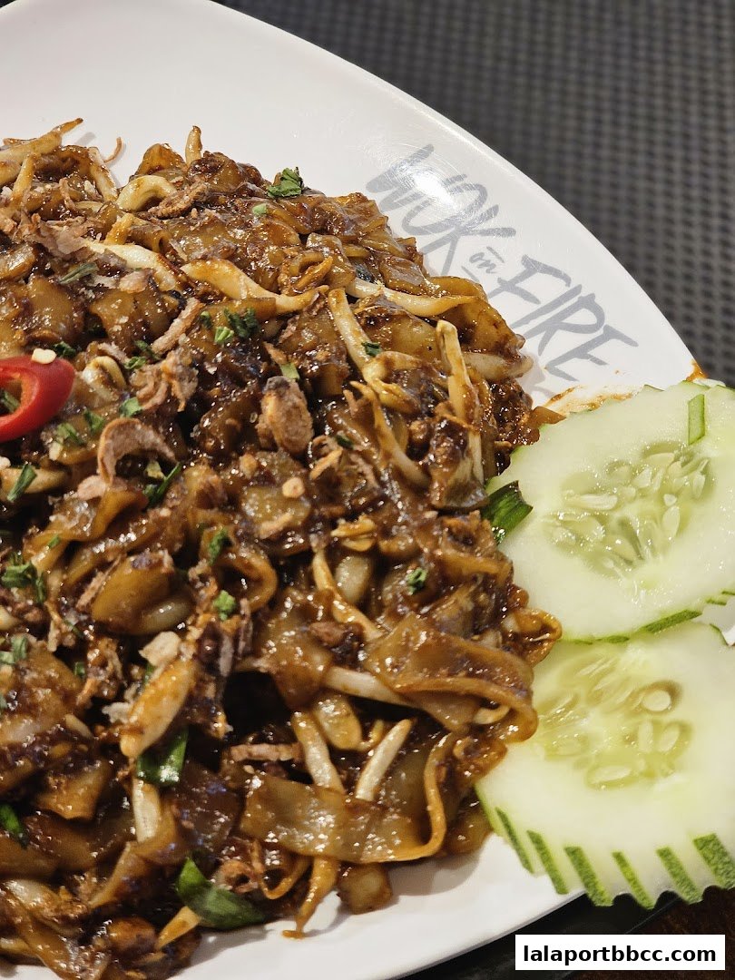 A close-up of a delicious plate of stir-fried noodles with chili and cucumber garnish.
