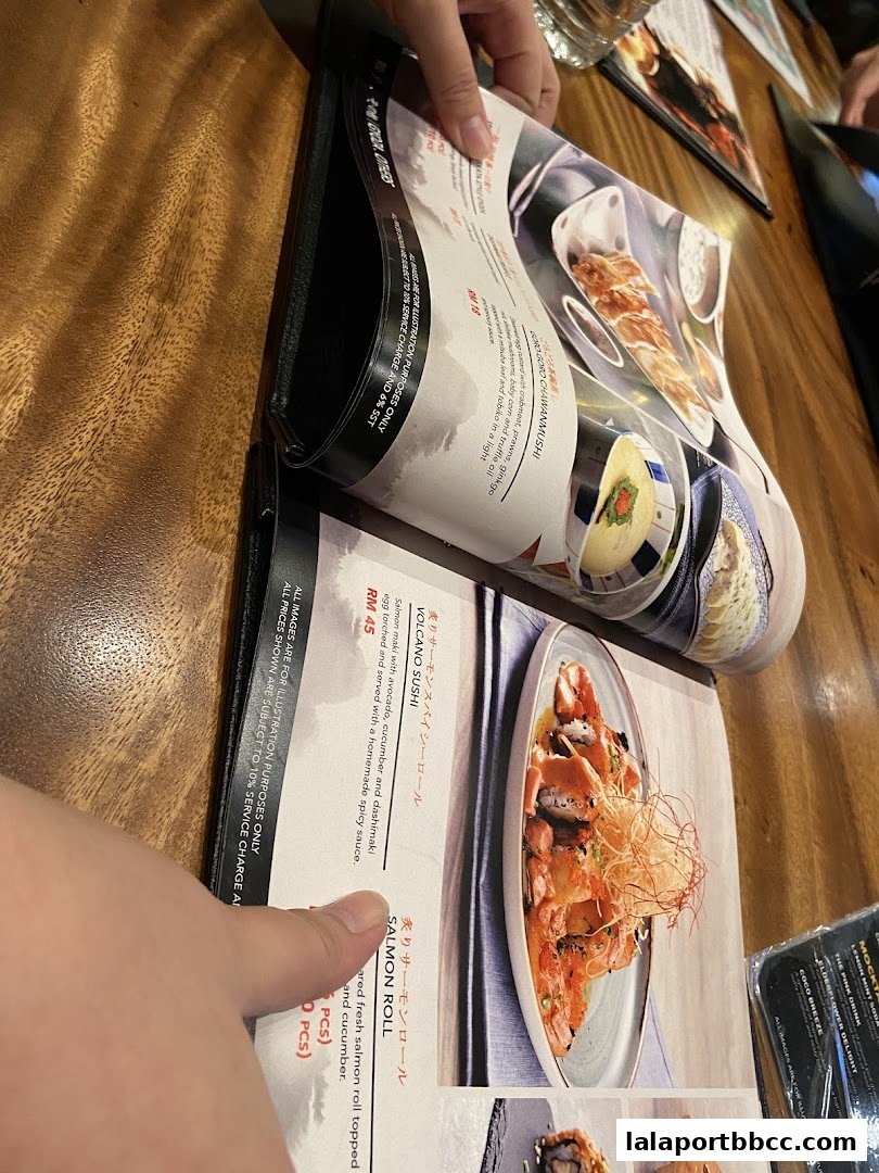 A person's hand pointing at a menu with pictures of sushi dishes.