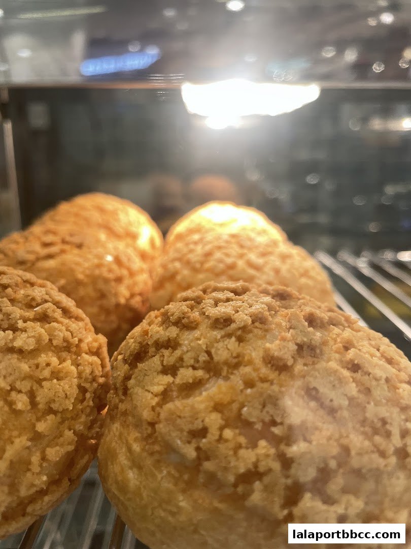 Close-up of golden-brown cream puffs with a crunchy topping in a display case.