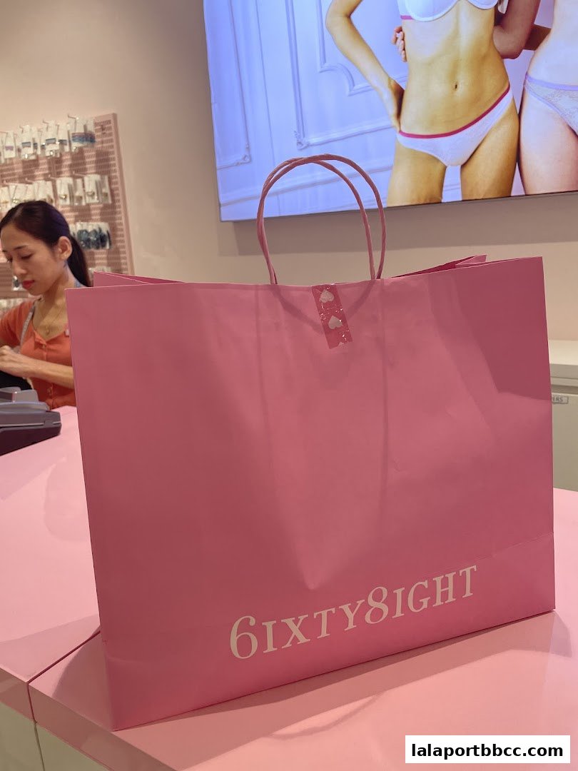 A pink shopping bag with the 6IXTY8IGHT logo sits on a pink counter in front of a display.