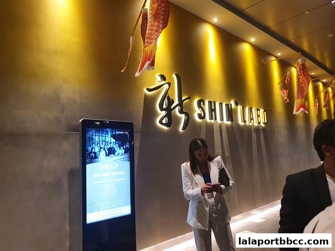 A stylish interior with a glowing sign for ShinLabo and a digital display showing a hiring advertisement.