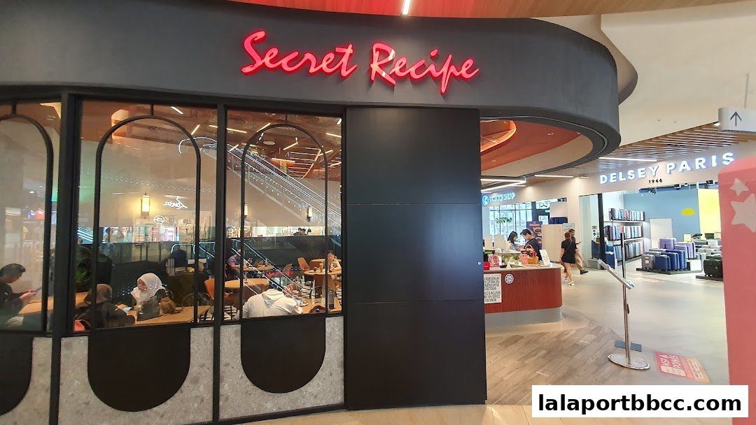 The exterior of a Secret Recipe cafe with customers seated inside and a neighboring Delsey Paris store.