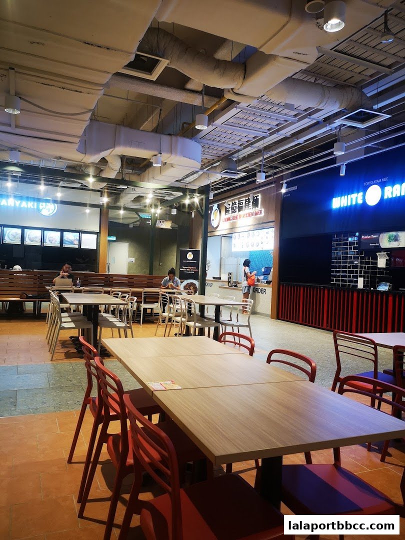 A food court with tables and chairs, featuring various food stalls including Loong Kee Hokkien Mee.