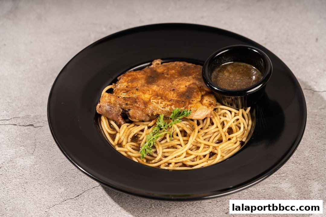 A plate of spaghetti topped with a grilled chicken chop and a side of gravy.