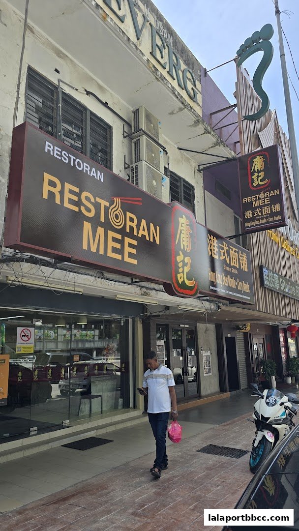 The exterior of a Hong Kong-style noodle shop with prominent signage and a pedestrian walking by.