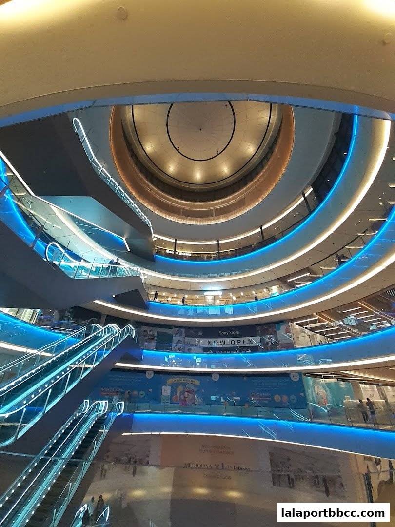Modern shopping mall interior with escalators and illuminated blue railings.