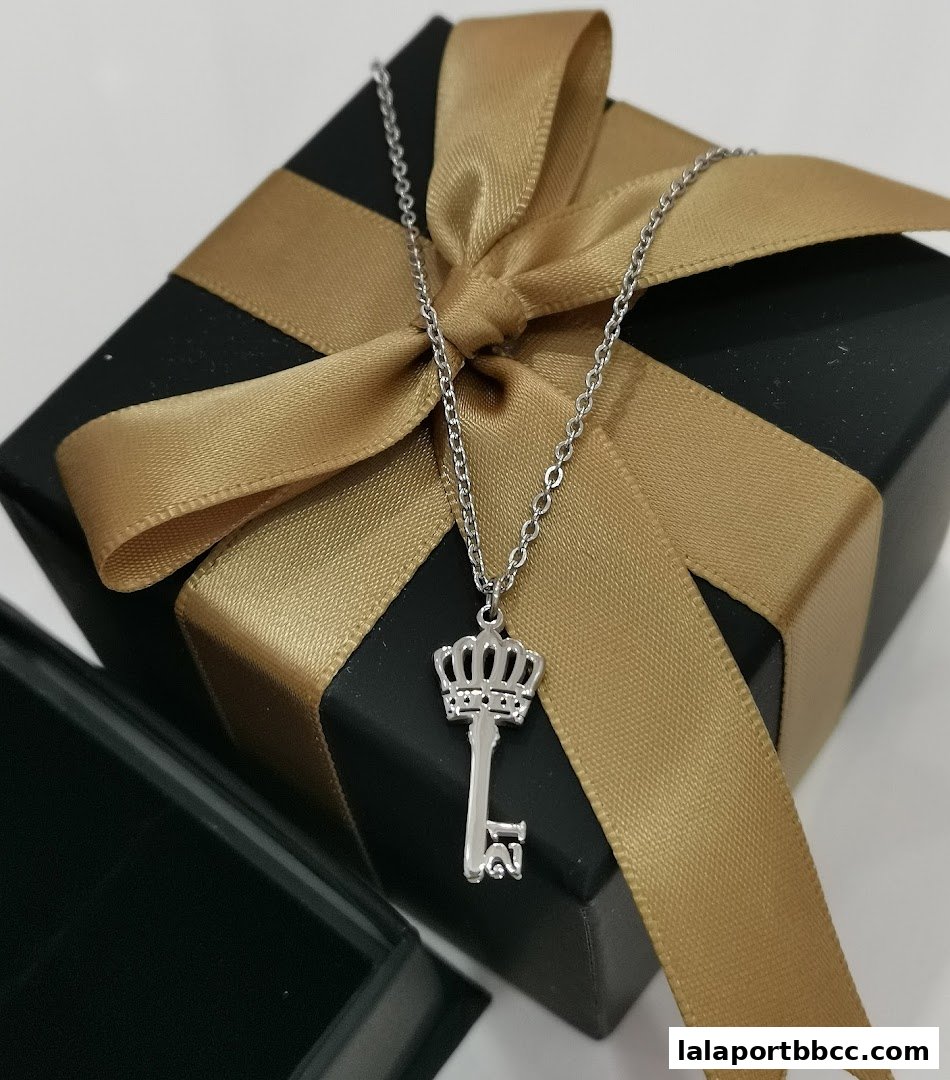 A silver necklace with a key pendant rests on a black gift box with a gold ribbon.