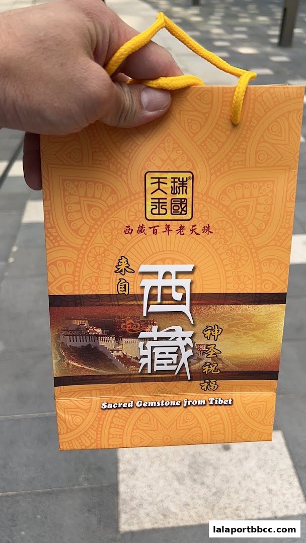 A hand holds an orange paper bag with Tibetan imagery and text advertising sacred gemstones.