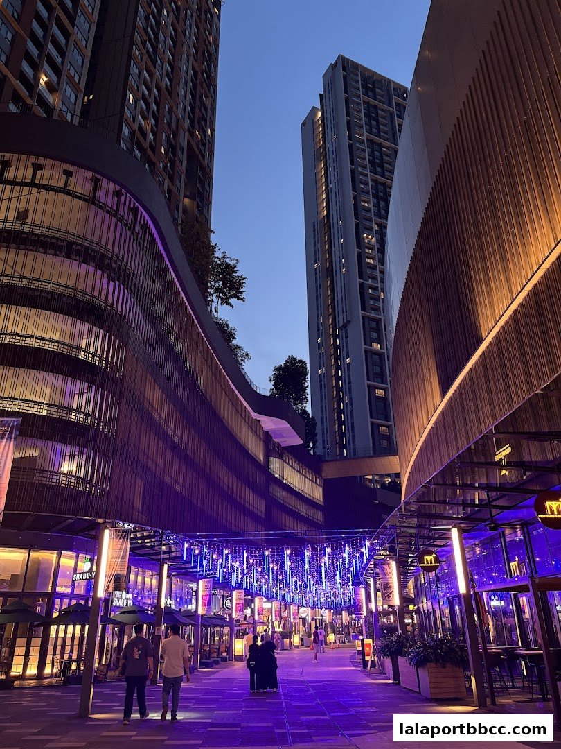 A vibrant street scene at Gourmet Street, Lalaport BBCC, illuminated by colorful lights at dusk.