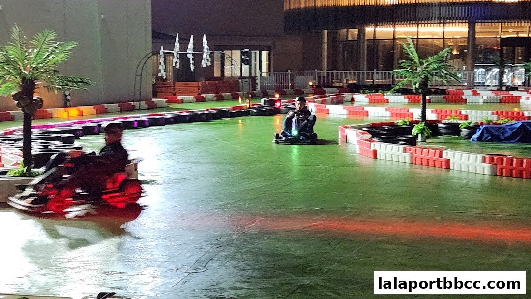 People racing go-karts on an indoor track with colorful lighting and palm trees.