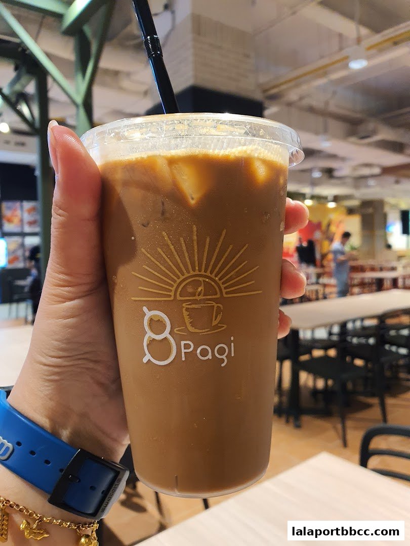 A hand holds a refreshing iced coffee with the Pagi logo visible.