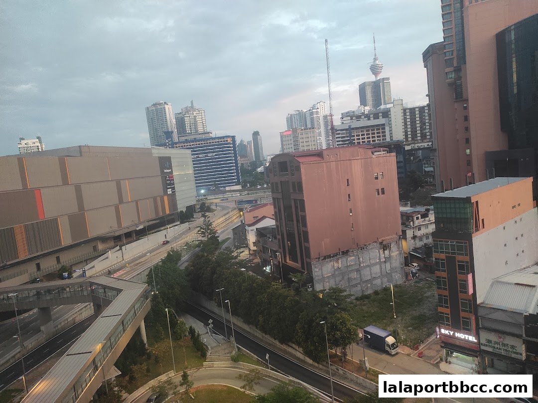 A cityscape view showing buildings, a mall, and a linked bridge under a cloudy sky.