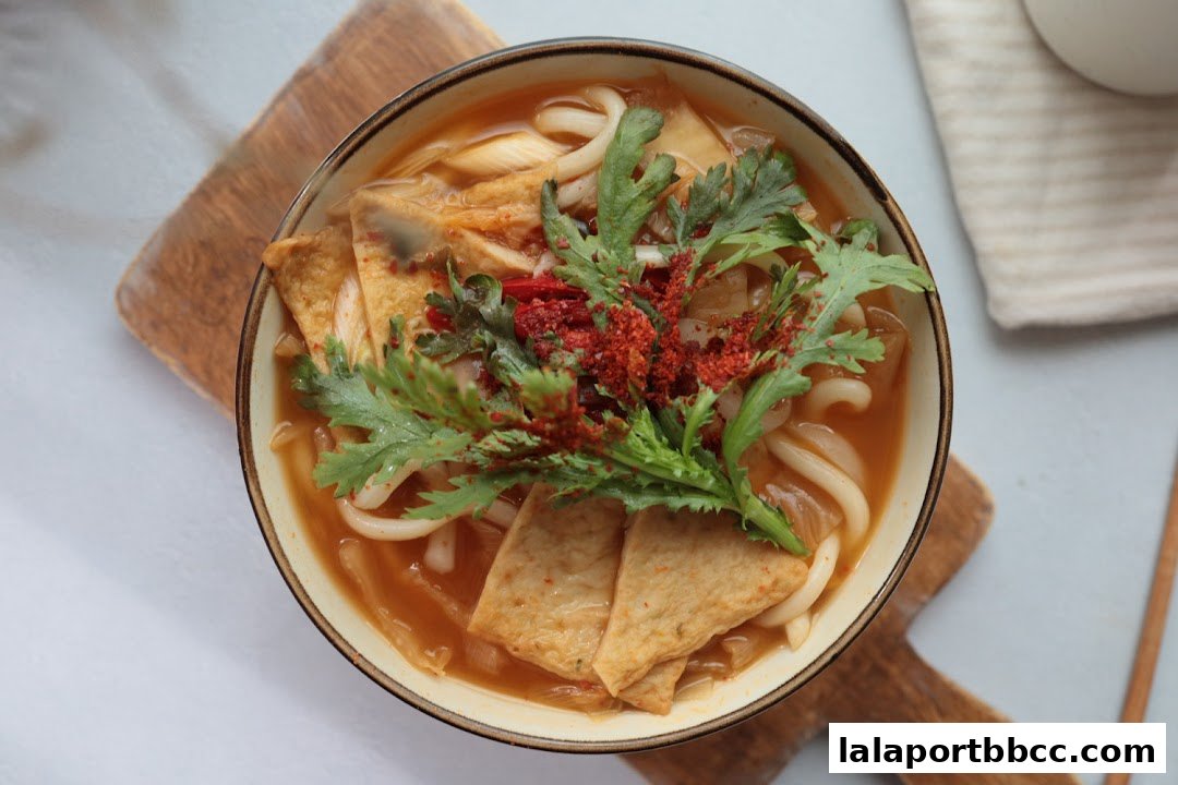 A top-down view of a steaming bowl of udon noodles with fish cakes and fresh greens.
