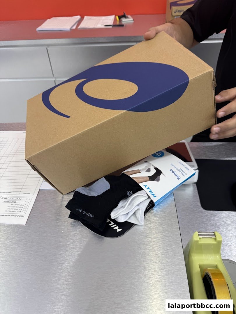 A person is holding a shoebox with a large blue logo and a pair of Hilly socks.