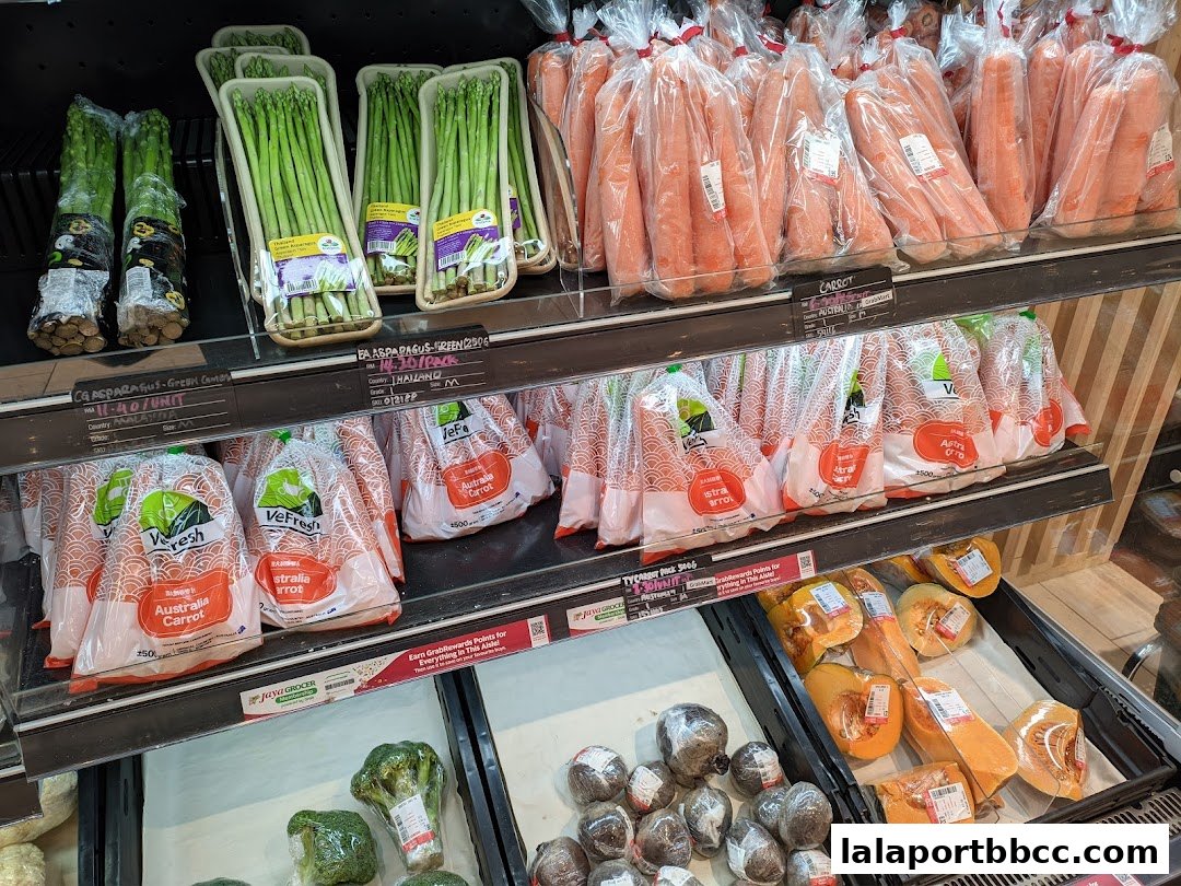 Fresh produce including asparagus, carrots, pumpkins, and broccoli displayed on shelves at Jaya Grocer.