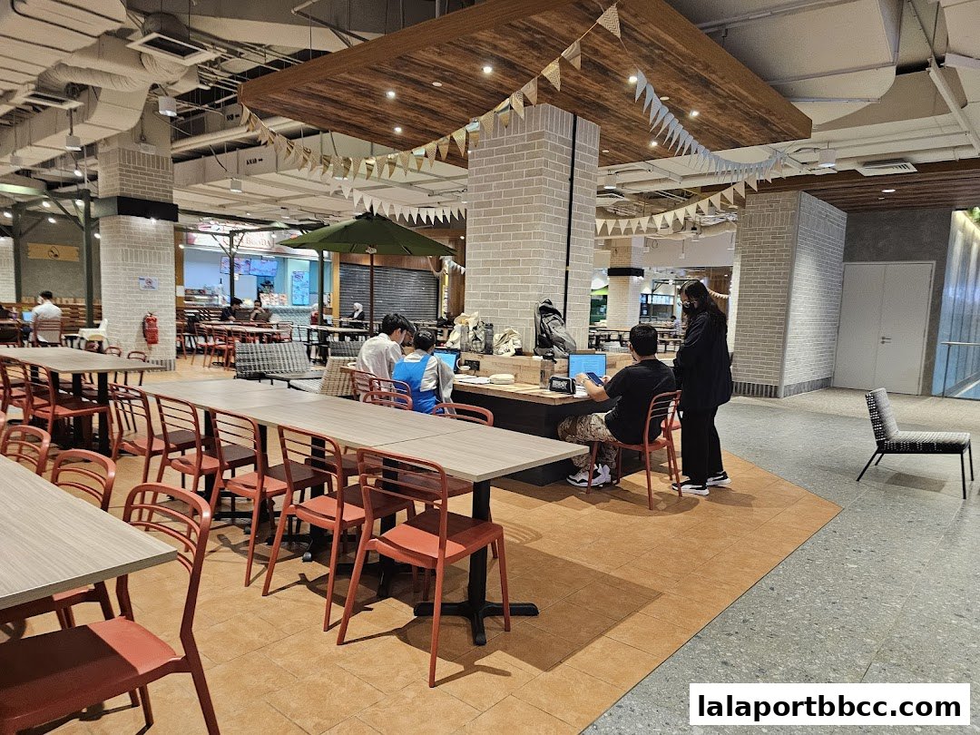 A spacious food court with multiple dining tables and chairs, and people interacting.