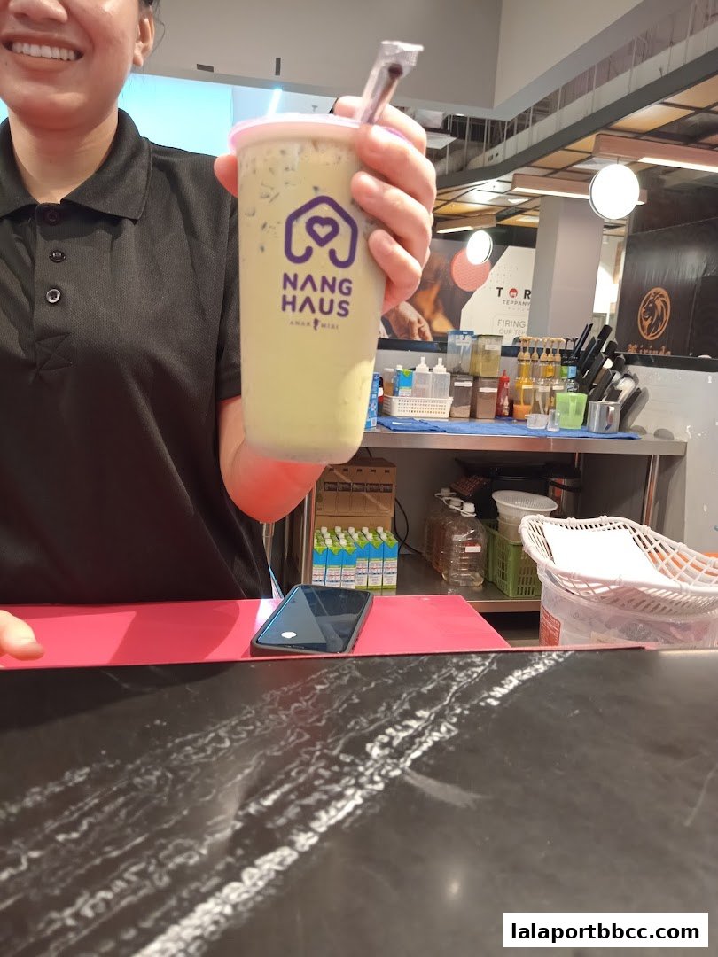 A person holds a green beverage with the Nang Haus logo in front of a counter.