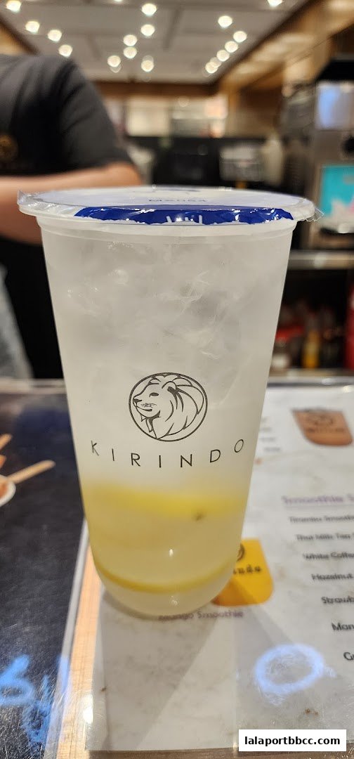 A close-up of a refreshing drink with the Kirindo logo and a blurred menu in the background.