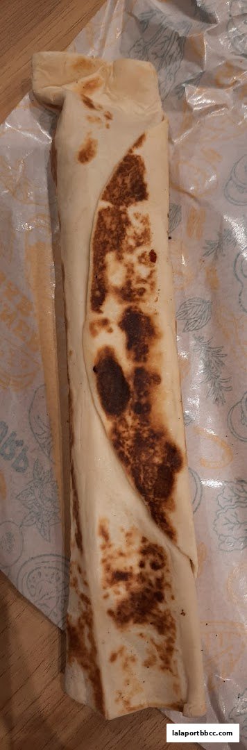 A close-up shot of a large, grilled kebab wrap on branded paper.