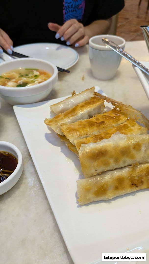 A plate of golden-brown pan-fried dumplings served with a small bowl of dipping sauce and a bowl of soup.